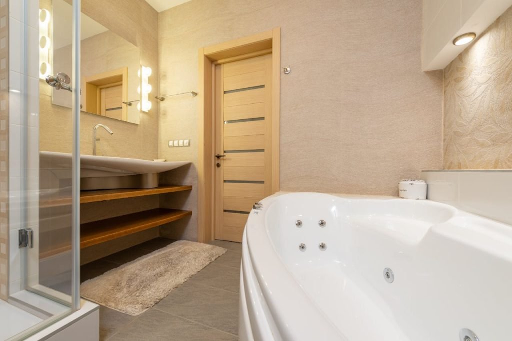 Interior of modern bathroom with shower near bath and sink on cabinet under mirror next to door